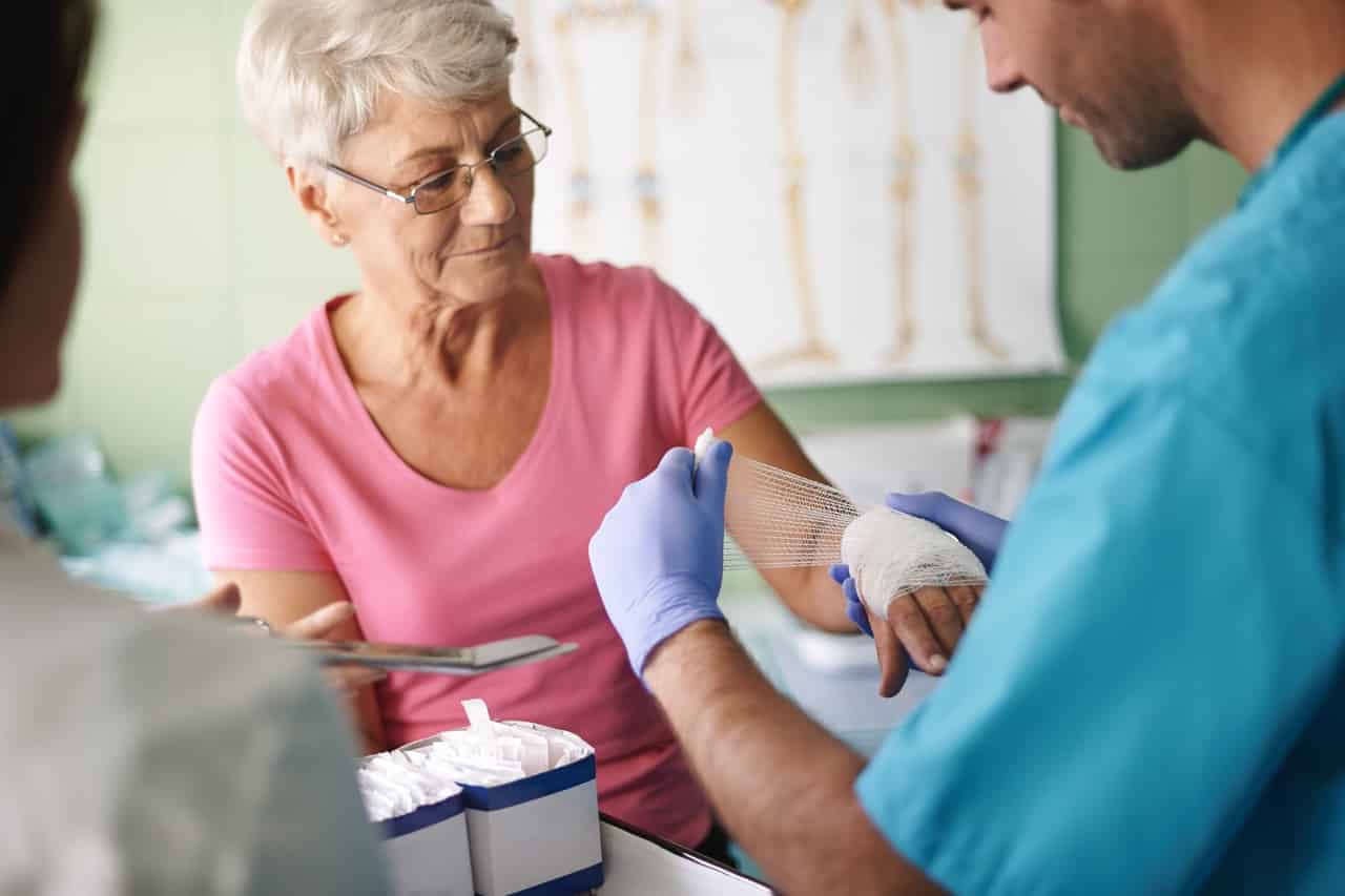 A nurse putting a bandage on an elderly woman's hand in a skilled nursing facility