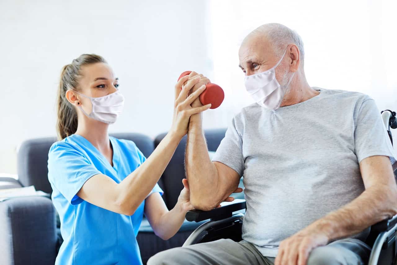 A nurse helping an elderly man with physical exercises in a senior rehabilitation facility