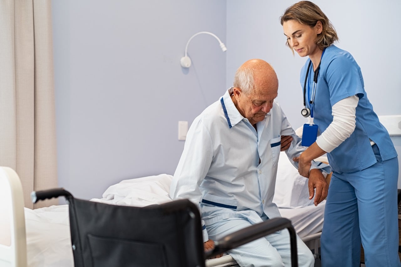 Nurse gently supporting an elderly man to get up from bed