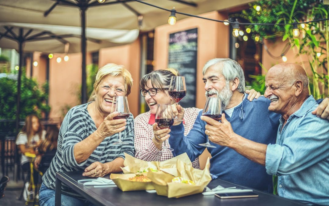 Happy elderly friends toasting with glasses of red wine sitting at a bar in the city streets - Mature people having fun celebrating in the time of happy hour - Food, drink, retirees concept